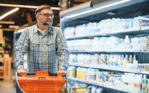 Homem realizando compras no mercado e observando a embalagem dos produtos.